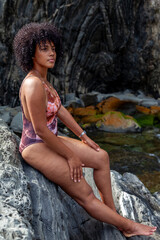 Obraz premium Young woman with natural curly hair relaxing on rocks by the ocean
