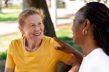 Diverse senior women friends share a joyful outdoor conversation, one smiling brightly while the...