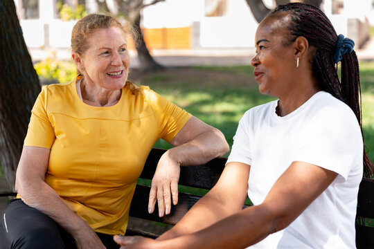 Diverse senior women friends enjoying outdoor conversation on a park bench, sharing smiles and connection, promoting aging gracefully and community