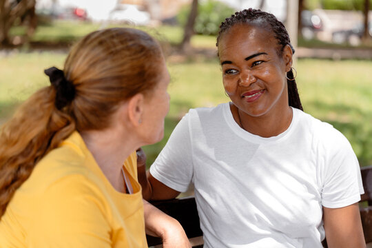 Smiling african american woman engaging in a warm conversation with a friend outdoors, sharing moments of diverse friendship and active listening in a park setting