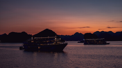 Cruise ships anchored in Ha Long Bay at deep sunset, dramatic orange and purple sky over the water