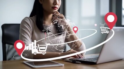 Focused asian woman works on laptop at wooden desk with global logistics graphics in a bright room. Logistics, worldwide delivery and business concept. - Powered by Adobe