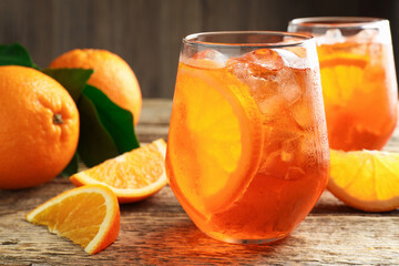 Glasses of refreshing spritzer cocktail and oranges on wooden table, closeup