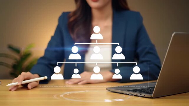 Professional woman in blue suit drawing an organization chart near a laptop on a wooden desk, illustrating business structure and leadership concepts.