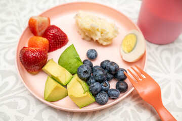 Kids dinner on a pink plate, picky eaters dinner with avocado, strawberries, mashed potatoes, egg and blueberry. Healthy dinner option. 