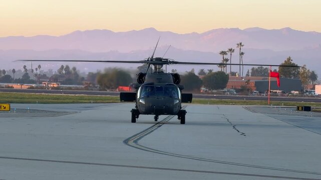 Nose-on view of a black helicopter idling on the ground at sunset.