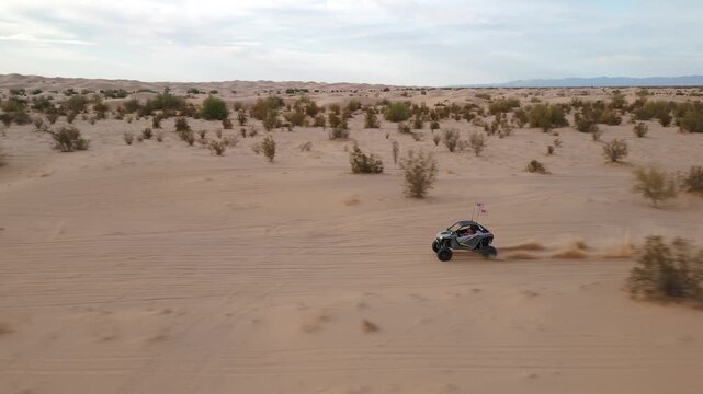 Aerial view of Polaris RZR UTV driving through desert sand dunes at sunset.