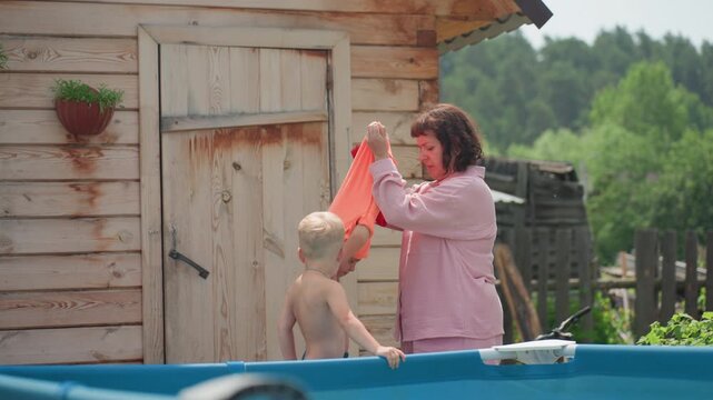 Child Wearing Floaties By Pool, Mother Secures Floatation Devices For Child, An Outdoor Scene With Child In Flotation Devices, Mother Ensures Her Son Wears Safety Floaties At Swimming Area