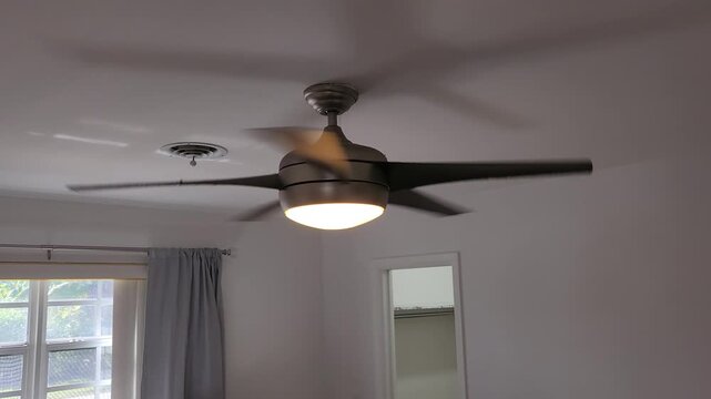 Modern silver ceiling fan with light on spinning smoothly at medium speed indoors