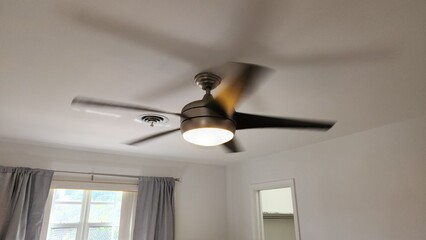 Ceiling-mounted silver fan with light on, static photo of modern indoor ceiling fan