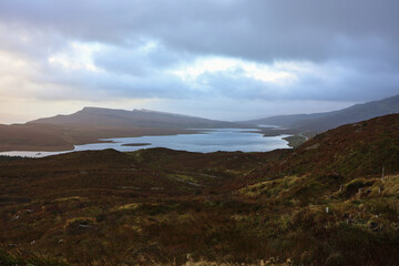 Golden hour view over Loch Leathan from above, scenic Isle of Skye landscape with tranquil water, rolling hills and warm light near the Old Man of Storr