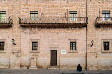 Young man sitting in front of the historic Archbishopric building entrance with iron balconies in Morelia, Mexico