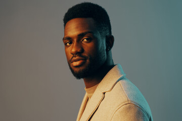Stylish portrait of a young Black man in a light grey blazer, showcasing confidence and a modern aesthetic with soft blue background hues