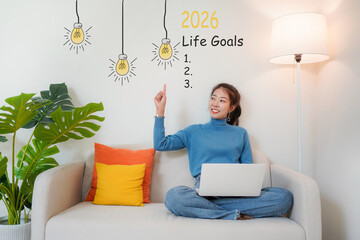 2026 Life Goals.  Young woman pointing cheerful and happy new year with laptop on the sofa in living room.  Star together new year 2026