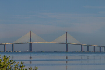 the iconic Sunshine Skyway Bridge spanning Tampa Bay, Florida under a dramatic blue sky. Warm sunset light and sweeping clouds highlight the modern architecture and elegant engineering of this famous 