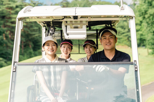 Male and female golfers riding golf carts at a golf course - Powered by Adobe