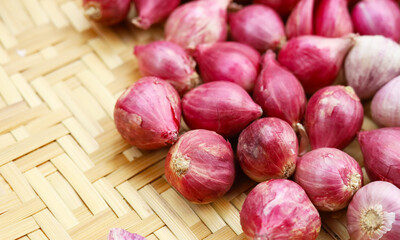 Fresh red shallots with single clove garlic bulbs on bamboo tray
