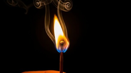 Close-up of a lit matchstick with a bright flame and smoke against a dark background.