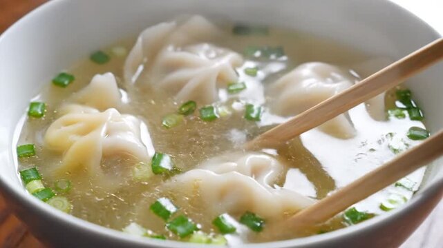 Wontons in clear broth with green onions and chopsticks.