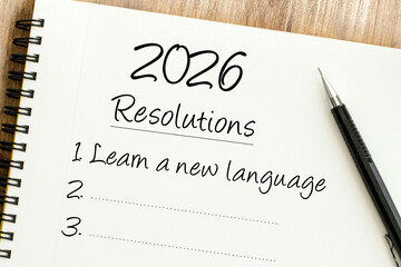 Handwritten 2026 Resolutions list in a spiral notebook with Learn a new language as the first goal and a pen.