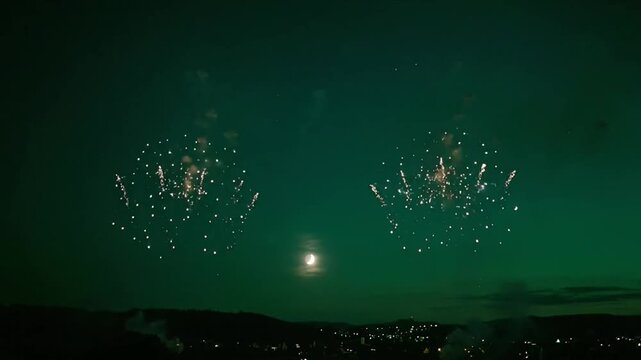 Festive Fireworks Exploding Over Town at Night with Moon Visible