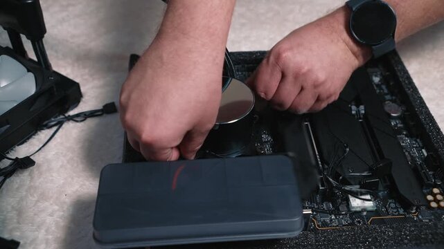 Male hand carefully presses the round water block from the liquid cooling system onto the CPU mounted on the motherboard, preparing it for fixation