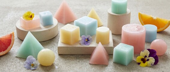 A colorful collection of pastel geometric candles and fruit slices creates a serene and inviting visual, exuding an ambiance of tranquility, beauty, and creative interior design.