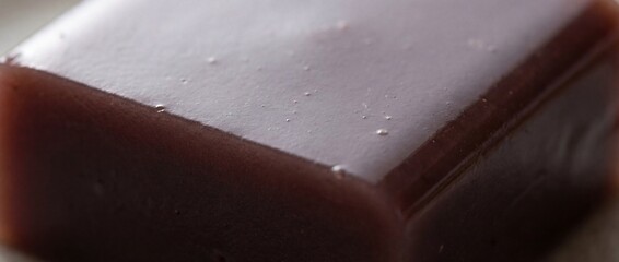 A close-up captures a translucent, vibrant cube of traditional Japanese dessert. The smooth, glossy surface reflects subtle light, inviting a moment of sweet contemplation.