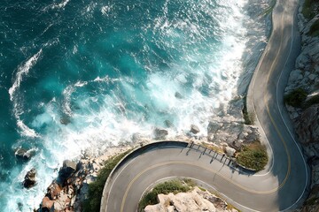 Aerial view of a winding coastal road next to turquoise ocean waves crashing against rocky shoreline. Travel concept along a scenic route by the sea.