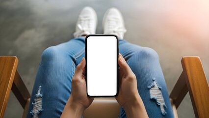 Person holding a modern smartphone with a blank white screen while relaxing in a wooden chair wearing ripped jeans
