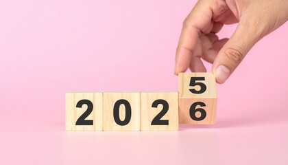 Wooden blocks displaying the year 2026 with a hand changing the final digit from 5 to 6, symbolizing the transition into the new year