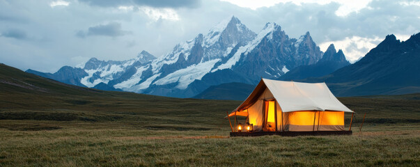  cozy tent illuminated at dusk, set against majestic mountains and expansive grassy terrain, capturing the beauty of nature and outdoor adventures.