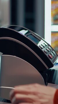 Vertical screen, close up of a cashier's hands operating a point of sale terminal, entering the price of goods, and accepting a contactless payment from a customer in a retail environment