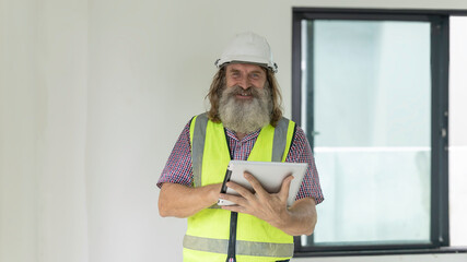 Experienced bearded construction foreman uses a digital tablet inside a new house, checking plans and managing the modern building project with confidence, precision and smart technology
