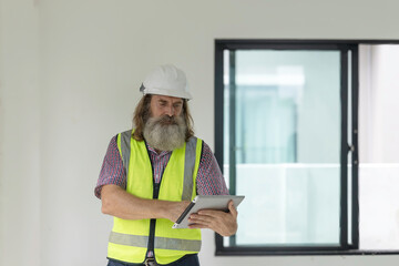 Experienced bearded construction foreman uses a digital tablet inside a new house, checking plans and managing the modern building project with confidence, precision and smart technology
