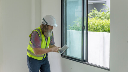 Experienced bearded construction foreman uses a digital tablet inside a new house, checking plans and managing the modern building project with confidence, precision and smart technology