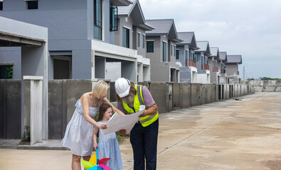 Senior construction foreman with beard using blueprint to explain a mother and her daughter for the detail of house building during the site check.