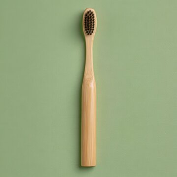 A single eco friendly bamboo toothbrush with black charcoal bristles is positioned vertically against a light green textured surface.