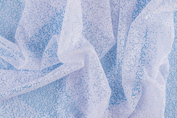 Background image of chaotic waves of openwork white fabric with floral ornaments. Abstract background of white guipure. delicate texture of folds