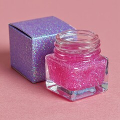 A close up studio shot of an open glass jar filled with shimmering pink glitter cosmetic product next to its glittery purple box packaging on a textured pink surface.