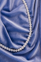 Elegant festive vertical background of velvet fabric with pearl white beads. A string of pearl beads among the soft folds of velvet. top view.