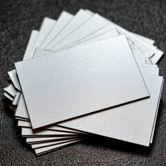 A close up overhead shot of a fanned stack of blank silver glitter business cards resting on a dark textured surface.