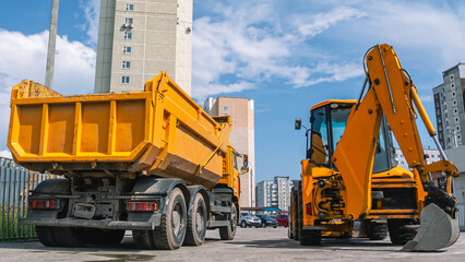 Road construction equipment. Dump truck for transportation of construction goods. A big truck with a body. Excavator-bulldozer-loader. Construction of buildings and roads.