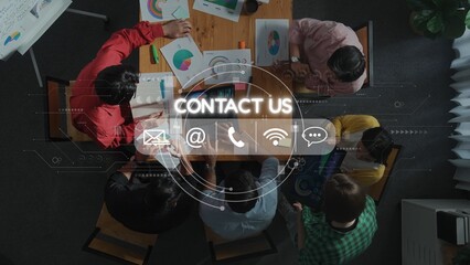 A group of diverse professionals engaged in a brainstorming session around a table filled with charts and graphs. The image features a contact us overlay, emphasizing communication. Raster