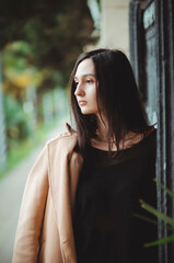 A young, beautiful woman wearing a beige coat on a city street. Close-up, profile portrait.