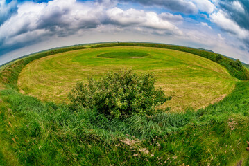 Fisheyeaufnahme des mit Gras &uuml;berwachsenen Ringwall der "Lembecksburg" auf der Nordseeinsel F&ouml;hr, mit einem Busch bei aufgelockerter Wolkendecke