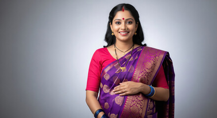 A radiant pregnant Indian woman in a rich purple and pink silk saree smiles gently while cradling her baby bump