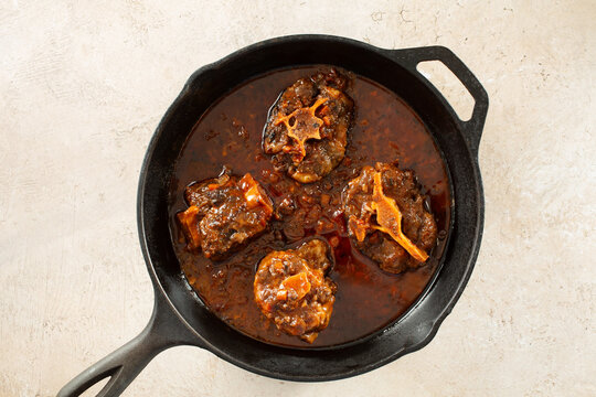 A top down view of braised oxtails in a cast iron skillet.