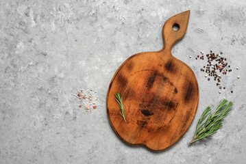 An empty round wooden cutting board with spices and rosemary on a rustic gray background. Minimal culinary backdrop. Top view, flat lay, copy space.
