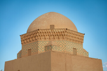 Decorative adobe dome of the Ziaieh School, also known as Alexander’s Prison, in Yazd, Iran. Intricate brick patterns and geometric motifs against a clear blue sky highlight Persian desert architectur © Contentino